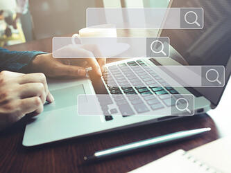 person using laptop overlaid with magnifying glass/search icons